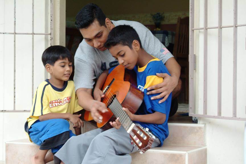 Father teaching his two sons how to play the guitar